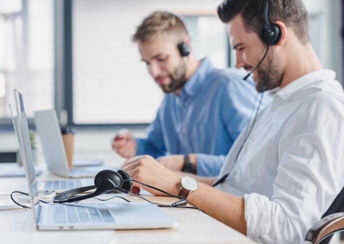 smiling-young-call-center-operators-in-headsets-using-laptops-in-office.jpg